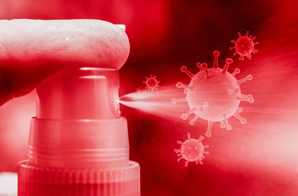 Finger pushing down on spray bottle attacking animated virus cells in the air.